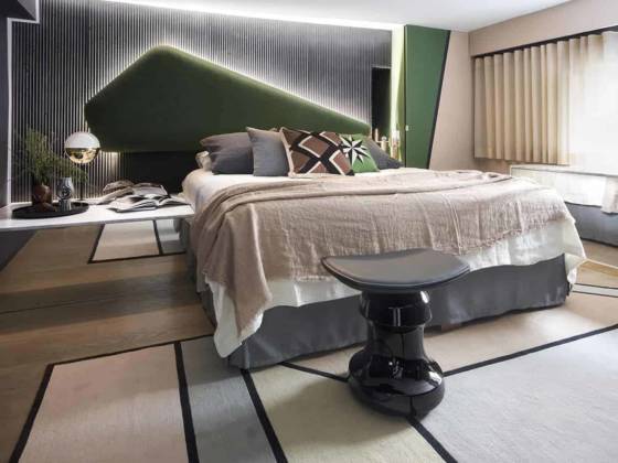 En haut, la chambre laisse exprimer une explosion de couleurs. Elle joue avec une rigueur géométrique insufflée par la tête de lit réalisée sur-mesure qui contraste avec le revêtement filaire Panbéton® de Neri&Hu pour Concrete LCDA. Le bloc de chevet participe avec son jeu de miroir à décupler l’espace, dupliquant le tapis Visioni de Patricia Urquiola, CC-Tapis. Lampe de table 06 de Magic Circus. Jeté de lit en lin, Maison de Vacances. Coussins Lindell&Co et India Mahdavi pour Pierre Frey.