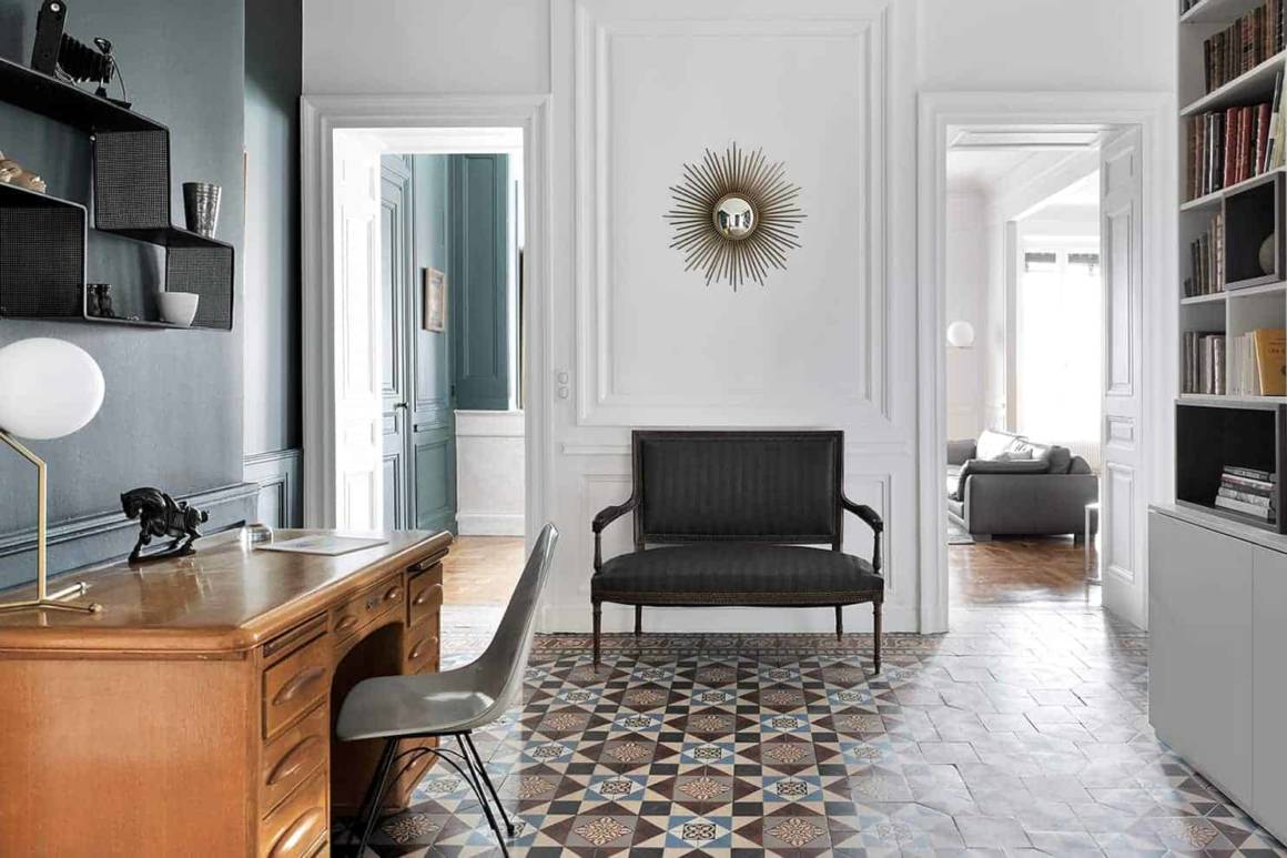 Entrée/bureau distribuant l'ensemble des espaces jour et nuit. Bibliothèque sur-mesure dessinée par l'architecte. Bureau et chaise chinés. Lampe à poser IC Lights T de Michael Anastassiades pour Flos, chez IF Contemporain. Étagère Dédal de Mathieu Matégot, Gubi. Miroir Soleil Chaty Vallauris. Peinture Silex de Ressource. En arrière plan, canapé Off Shore en cuir, de Roche Bobois