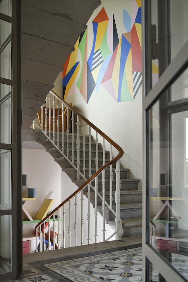Libéré de toutes entraves, l’escalier bénéficie de la lumière naturelle des ouvertures ajoutées. Oeuvre du graffeur lyonnais Poter. Bibliothèque chinée d’Ettore Sottsass pour Memphis Milano, en 1981. Papier peint Le Corbusier – Dots d’Arte