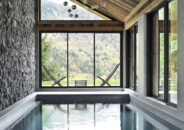 L’extension créée pour accueillir la piscine se connecte directement avec le paysage et le hot tub disposé sur la terrasse, comme suspendu dans le vide. Au mur, pierres naturelles posées une à une à la main, Sopierre. Suspensions, Bocci