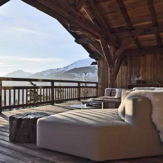 Sur la terrasse, blotti dans le canapé (Edra), à l’échelle de la vue, sous la voûte charpentée en mélèze vieilli, travaillée par les compagnons de Chalets Bayrou comme celle de Notre-Dame